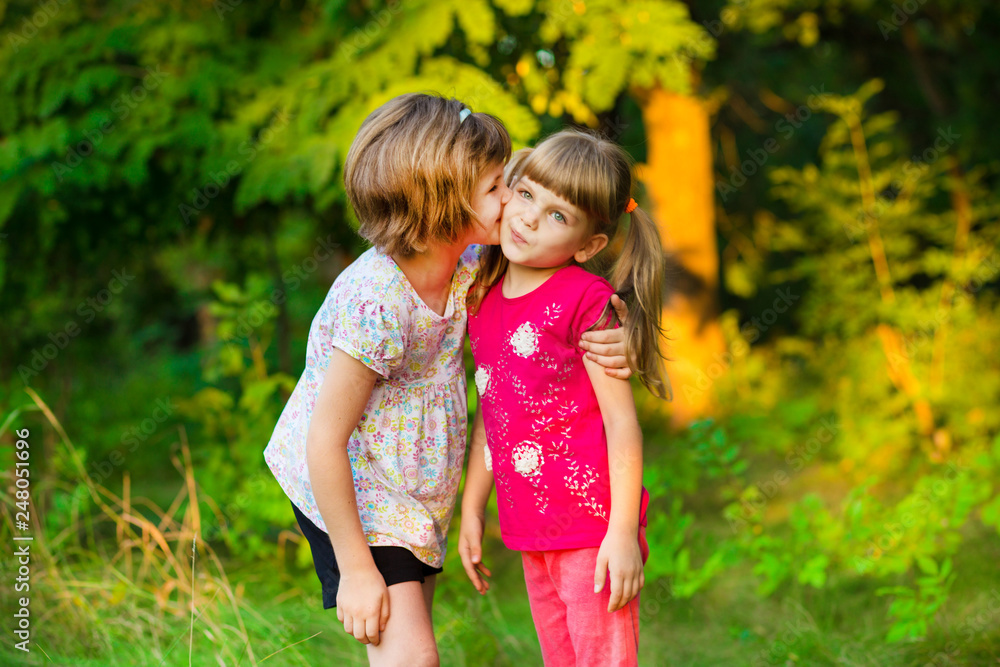 Two adorable little sisters laughing and hugging on sunny day in park Two adorable little sisters laughing and hugging on sunny day in park