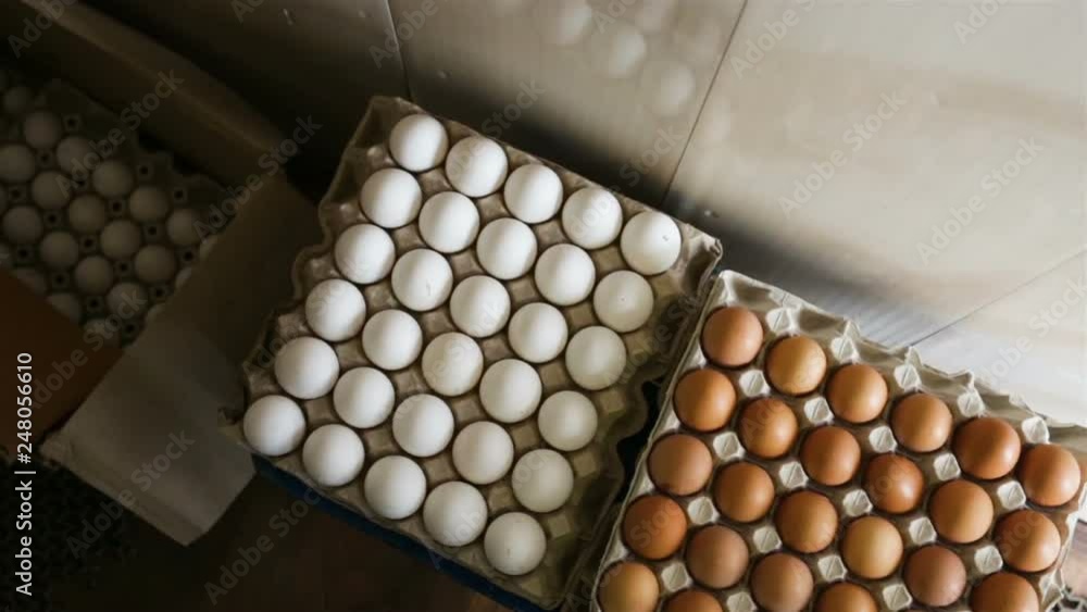 A large stack of packages of eggs is on the floor. Top view, camera movement from right to left, real time, natural light, indoors. A large stack of packages of eggs is on the floor. Top view, camera movement from right to left, real time, natural light, indoors.