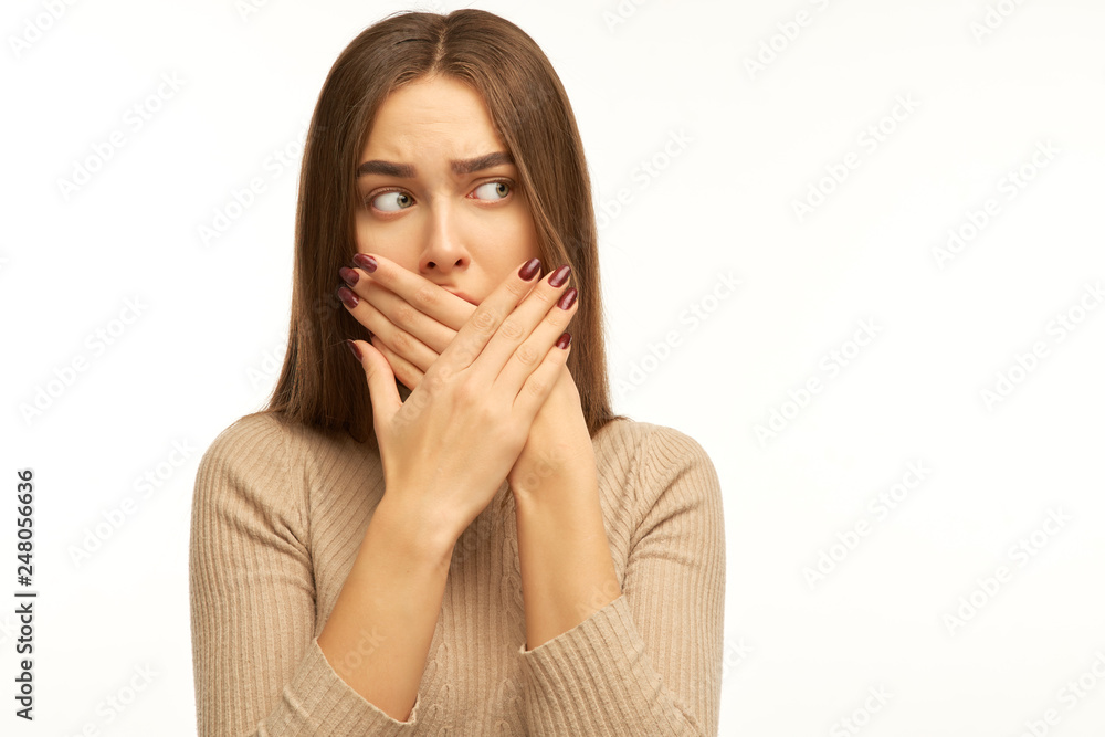 Incredulous attractive woman covers mouth, doesnt want to spread rumours, shocked to hear sudden news from interlocutor, dressed in casual sweater, isolated on white wall Incredulous attractive woman covers mouth, doesnt want to spread rumours, shocked to hear sudden news from interlocutor, dressed in casual sweater, isolated on white wall