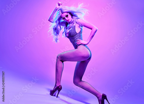 High Fashion neon light. Glamour Sexy girl with Trendy dyed wavy hair dance. Creative bright portrait beautiful woman, fashionable party outfit, heels. Pink purple neon color