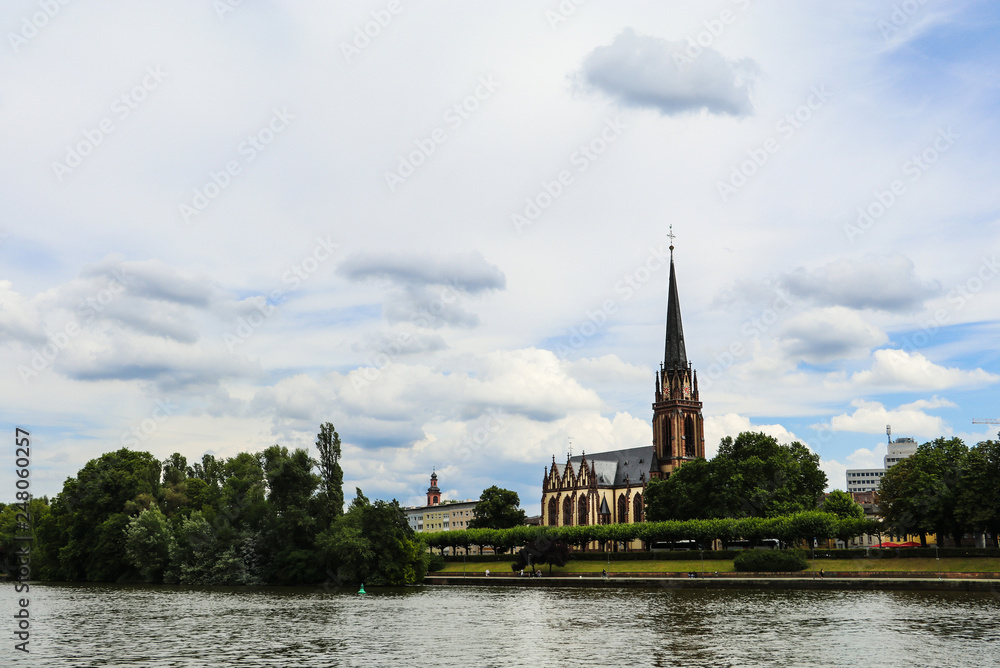Historical church between the trees near the river in Frankfurt am Main, Germany. City landscape photo with cloudy sky