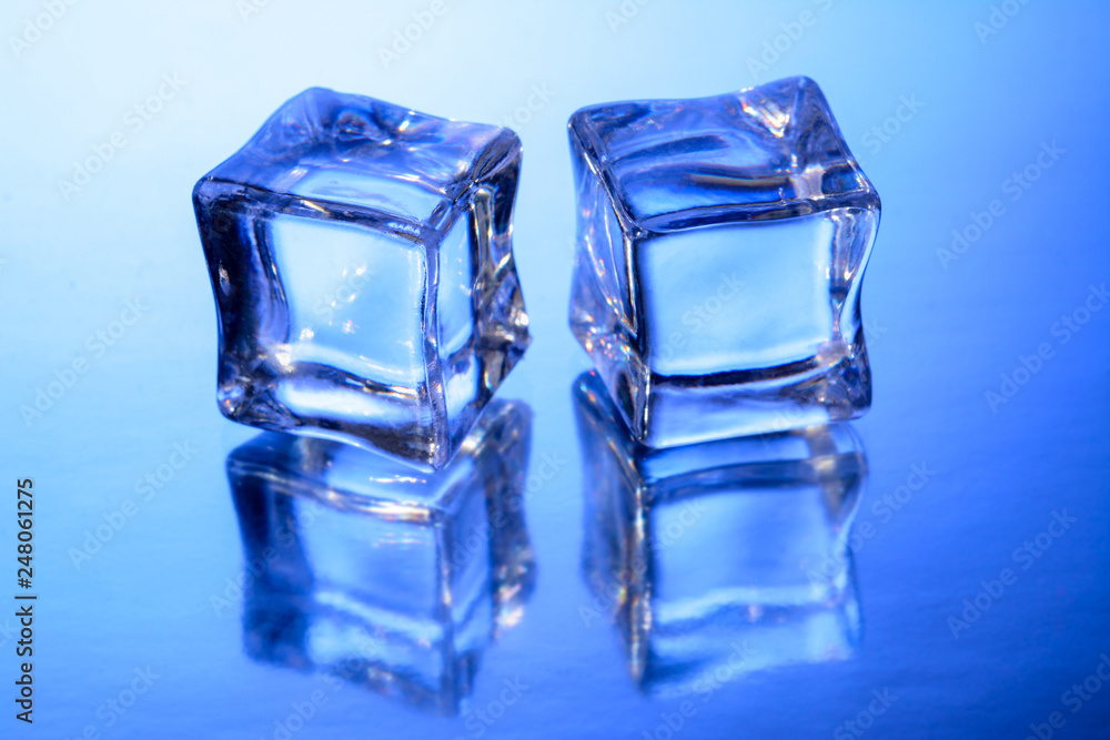 Two ice cubes on glass surface with blue gradient background. Two ice cubes on glass surface with blue gradient background.