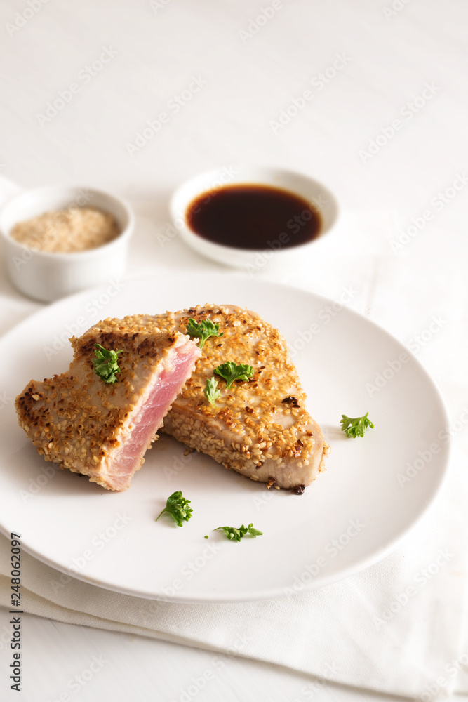 roasted tuna steak in sesame seeds with soy sauce on a plate on a white table, copy space, vertical roasted tuna steak in sesame seeds with soy sauce on a plate on a white table, copy space, vertical
