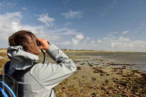 Frau mit Fernglas beobachtet Vögel am Wattenmeer photo