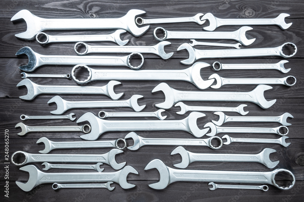 set of chromed wrenches on a dark wooden workbench. top view - obrazy, fototapety, plakaty 