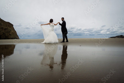 Adorable wedding couple walking along the beach, reflecting in the water. Panoramic view. © Vasyl Dovhun