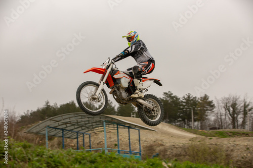 Racer on motorcycle participates in motocross cross-country in flight  jumps and takes off on springboard against sky. Concept active extreme rest.