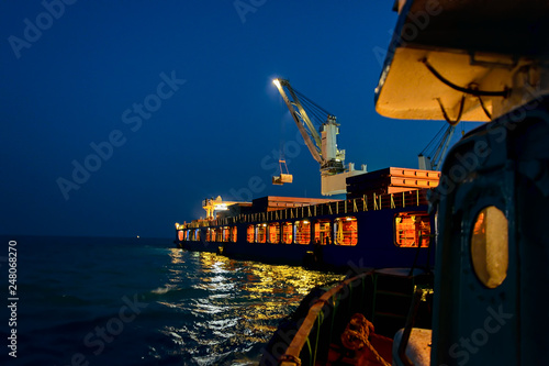Night loading big mother sea bulk carrier ship with Bauxite aluminium ore from the mini bulk carrier (feeder) vessel at offshore Kamsar port, Guinea, West Africa. photo