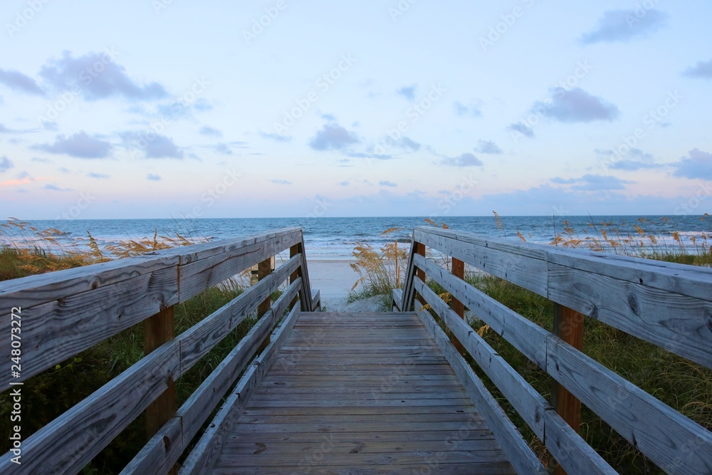 Fototapeta premium Beautiful landscape with way to the ocean beach. Wooden boardwalk and stairs to the Atlantic ocean beach over sand dunes in Huntington Beach State Park, Myrtle Beach area, SC, USA.