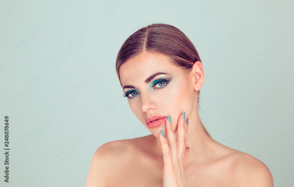 Sexy woman touching face with hand showing manicure in set with makeup. Attractive young model with blue green eye shadows make-up and manicure isolated on light green gray background. Sexy woman touching face with hand showing manicure in set with makeup. Attractive young model with blue green eye shadows make-up and manicure isolated on light green gray background.