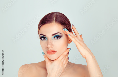 Sexy and sassy. Beautiful woman touching face with hands showing perfect makeup and soft skin, result of plastic cosmetic surgery, close up studio isolated on light green background.