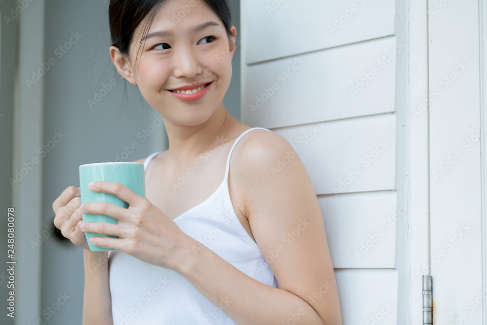 beautiful asian teen white Tank top happiness smile enjoy freshness morning with hot drink near window with sun light beautiful asian teen white Tank top happiness smile enjoy freshness morning with hot drink near window with sun light