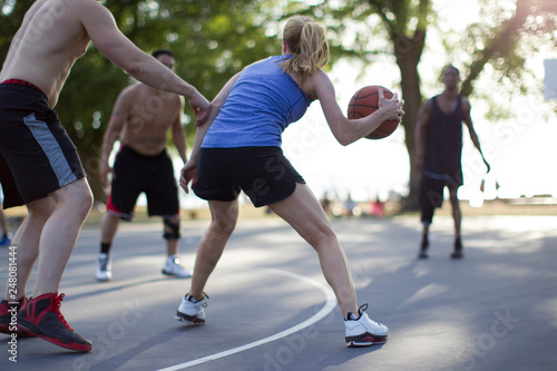 Grown woman playing basketball on outdoor court with male opponents. 