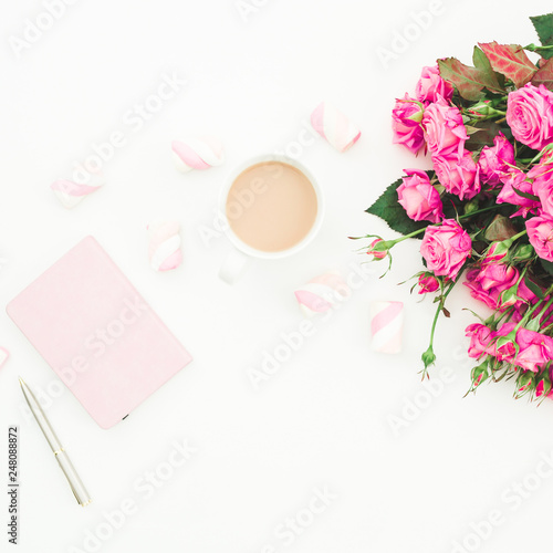 Female desk with pink roses bouquet, pink diary, coffee mug and marshmallows on white background. Flat lay. Top view