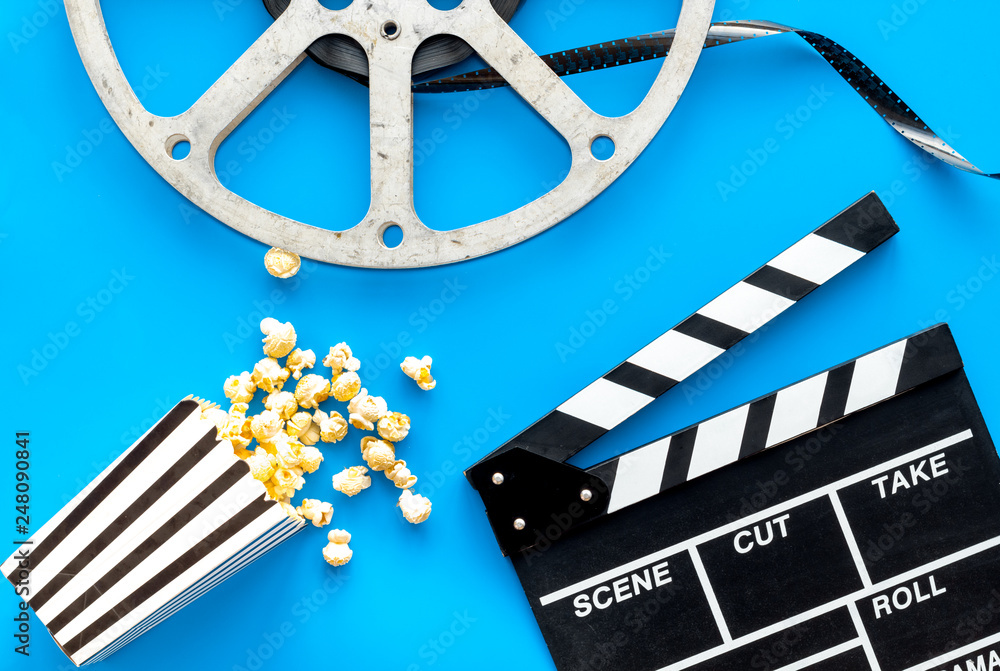 Cinema concept. Clapperboard, film stock, popcorn on blue background top view