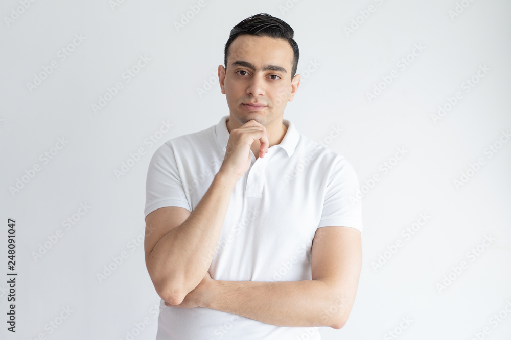 Pensive young man touching chin and looking at camera Pensive young man touching chin and looking at camera