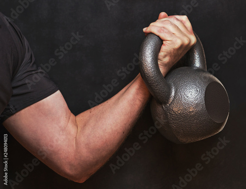 Kettlebell bicep curl, closeup of arm and hand working out with weights. Dark dramatic exercise photo for inspiration fitness over 40.