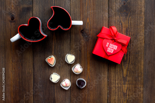 Valentine's day concept. Sweets, red gift box, heart-shaped mugs on dark wooden background top view