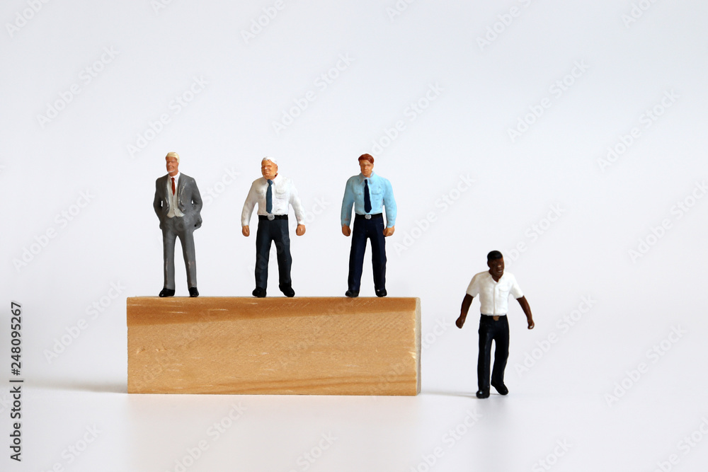 Miniature people standing on tree blocks and miniature man standing under tree blocks. The concept of racial discrimination in employment and promotion. Miniature people standing on tree blocks and miniature man standing under tree blocks. The concept of racial discrimination in employment and promotion.