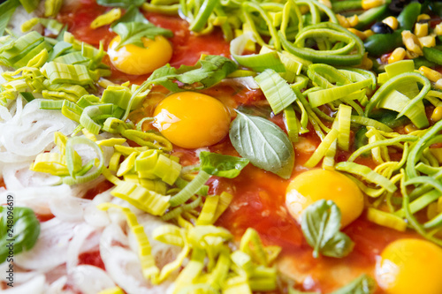 uncooked pizza with eggs, leek, ketchup, onion, basil, and other ingredients