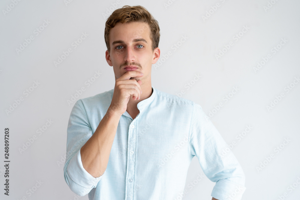 Pensive young man touching chin and looking at camera Pensive young man touching chin and looking at camera