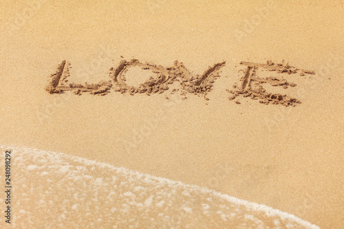 Word LOVE written in wet sand on the beach, sun shining over.