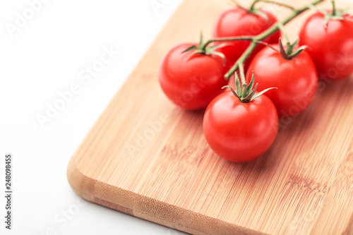 A branch of cherry tomatoes lies on a rectangular cutting board.