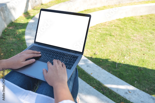 Mockup image of a woman using and typing on laptop with blank white screen , sitting in the outdoors with nature background