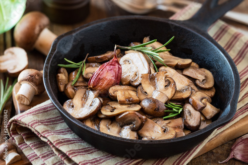 Cooked chestnut mushrooms or brown mushrooms in a cast iron skillet with rosemary and a clove of purple garlic photo