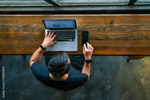 High angle view of Asian man working on smartphone and laptop