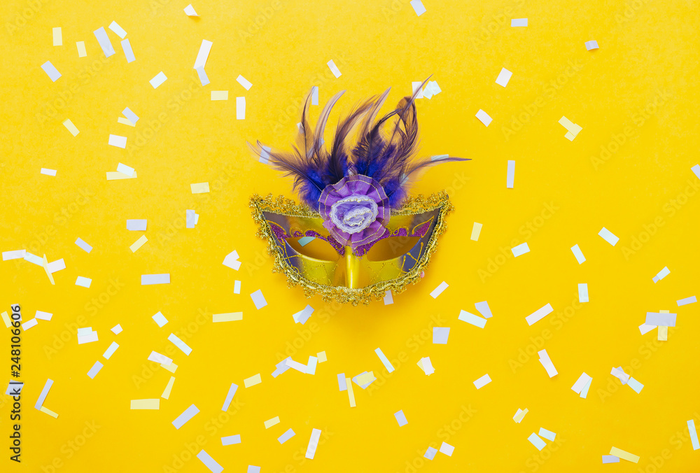 Table top view aerial image of beautiful colorful carnival season or photo booth prop Mardi Gras background.Flat lay object close up gold mask & confetti on yellow wallpaper.Space for text mock up. - obrazy, fototapety, plakaty 