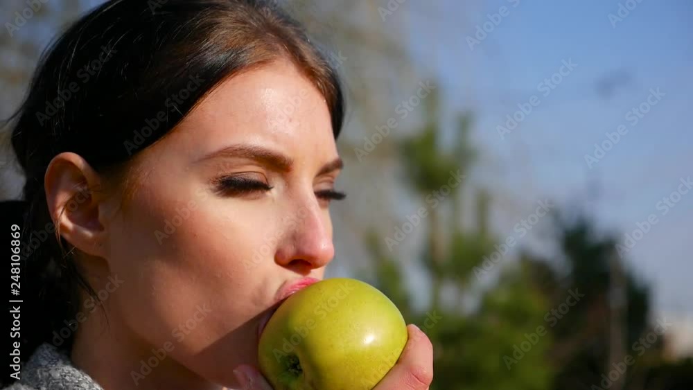 Slow motion, close-up attractive sexy young brunette woman with beautiful eyes and red lips eats green apple on sunny day. Spring beriberi, vitamins in fruits. Slow motion, close-up attractive sexy young brunette woman with beautiful eyes and red lips eats green apple on sunny day. Spring beriberi, vitamins in fruits.