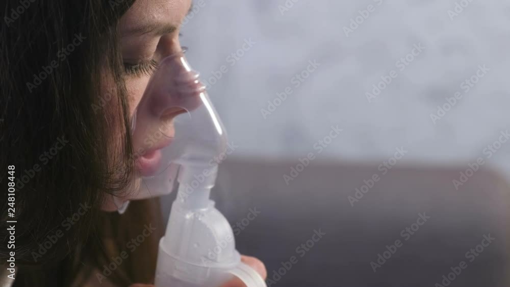 Use nebulizer and inhaler for the treatment. Young woman inhaling through inhaler mask. Close-up face, side view. Use nebulizer and inhaler for the treatment. Young woman inhaling through inhaler mask. Close-up face, side view.