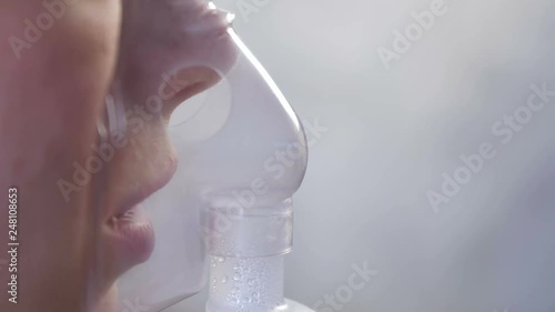 Use nebulizer and inhaler for the treatment. Young woman inhaling through inhaler mask. Close-up nose and lips in mask, side view.