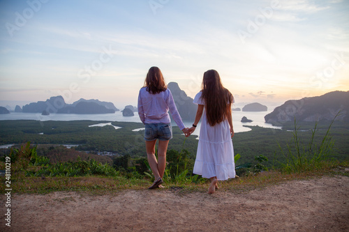 two girls hold hands against the backdrop of a stunning landscape of mountains