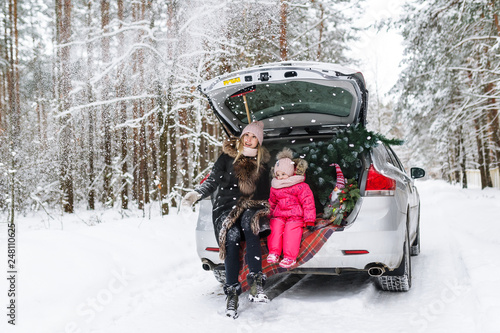 Obraz na płótnie Happy mother with the little daughter and Christmas tree sitting in the car in the winter forest w salonie