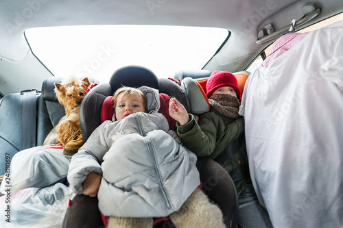 Obraz na płótnie Two children in warm clothes is in the car in wintertime. w salonie
