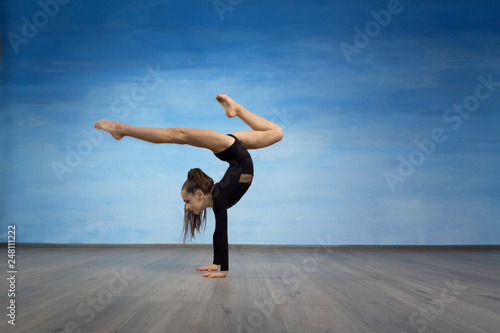 Girl gymnast in a black gymnastic swimsuit makes handstand on a blue sky background. photo