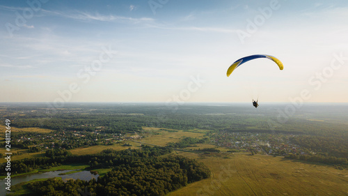Paraglider flies over green fields. High altitude. The athlete turns the thermal current. Rise up. Weather for flights. Top view of the paraglider flying over a green field with a road. 