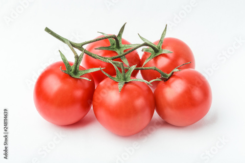 A branch of cherry tomato lies on a white surface.
