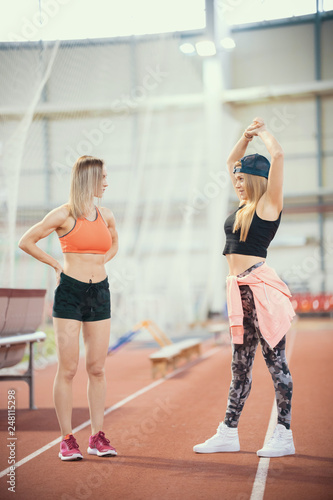 Two young athletic women stretching and warming up in sports arena