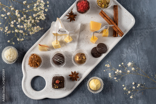 Set of fine chocolate candies and cheese. White, dark and milk chocolate, brie, blue cheese, goat cheese and parmisan on the plate. Chocolate cheese plate, top view. photo