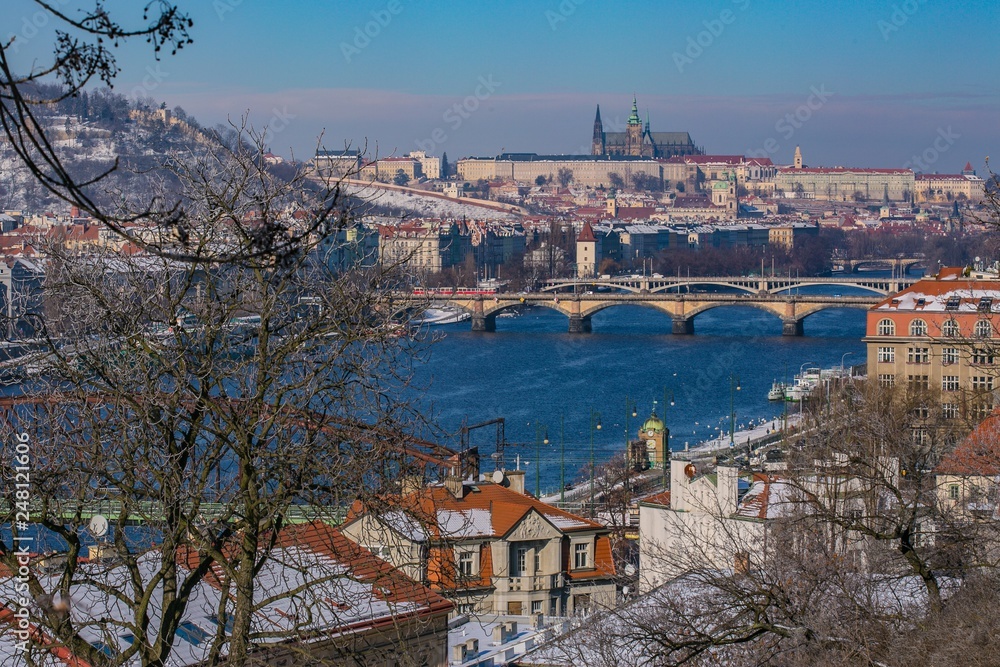 Prague, Czech Republic / Europe - February 5 2019: Scenic view of Prague city, Prague castle in distance, buildings and bridges across river Moldau, sunny winter day, clear blue sky