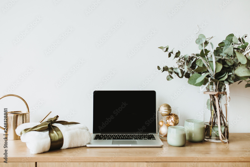 Fototapeta premium Blogger, freelance home office desk workspace. Laptop with mock up screen on wooden desktop decorated with eucalyptus bouquet, gift box, candles on white background.