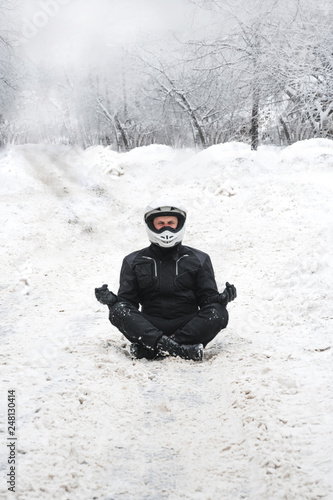 Rider man is sitting on snowy road alone. meditating in the lotus position that used to end the winter. travel tour, active life style concept. winter clothes, equipment, vertical photo