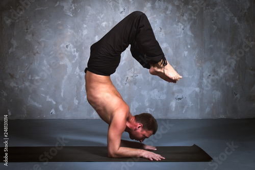 Young man performing a yoga pose Vrishchikasana photo