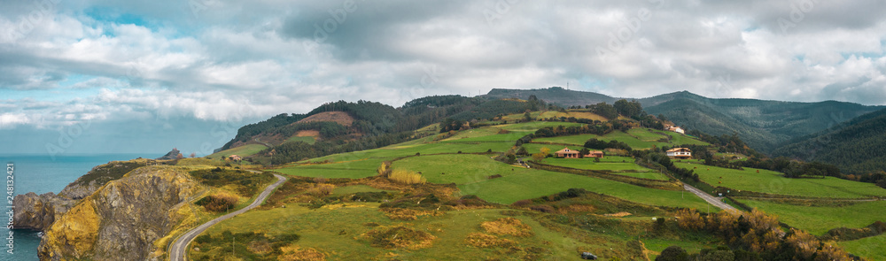 Aerial rural view of green fields and little villages on the hills; northen part of Spain; winter cloudy weather, evergreen plants and trees; fresh sea air, sun shining throug the dramatic sky, Bakio Aerial rural view of green fields and little villages on the hills; northen part of Spain; winter cloudy weather, evergreen plants and trees; fresh sea air, sun shining throug the dramatic sky, Bakio