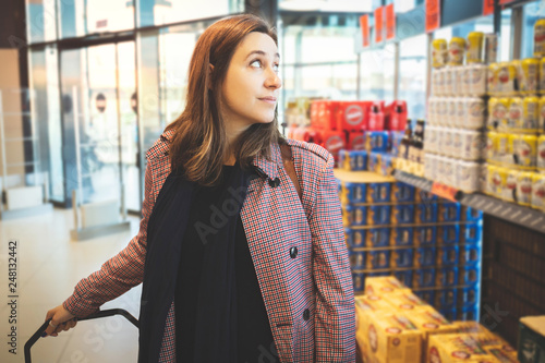 Woman at the supermarket making shopping choosing products showing her consumerism in the market with background and blurred marks. Girl looking at products pulling the cart inside the grocery store. © Daniel Rodriguez