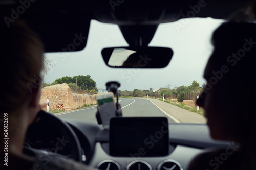 Selective focus on road. Close-up shot two female silhouettes traveling by automobile. Good view of long road with curves and signs. Young driver uses navigation on phone. Mock up for advertising.