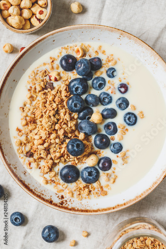 Top view on healthy breakfast, a bowl with organic granola, chocolate pieces, fresh blueberries, hazelnuts and soya milk.